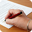 A hand wearing a silver bracelet holds a red metal pen while signing the bottom of a white paper form.
